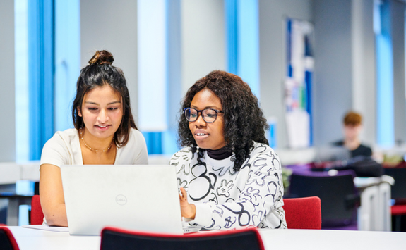 Two people sit at a desk looking at a laptop. The QS logo has been added to the image.